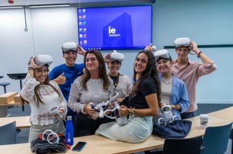 Group of students using VR headsets|Picture of six undergrad students looking and signaling to an AI white robot.|