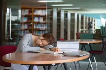 Tired,Woman,Student,Sleeping,On,Desk,In,Library.